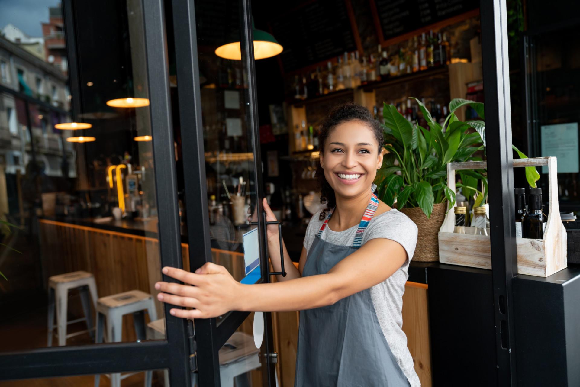 A woman opens the door to her cafe.